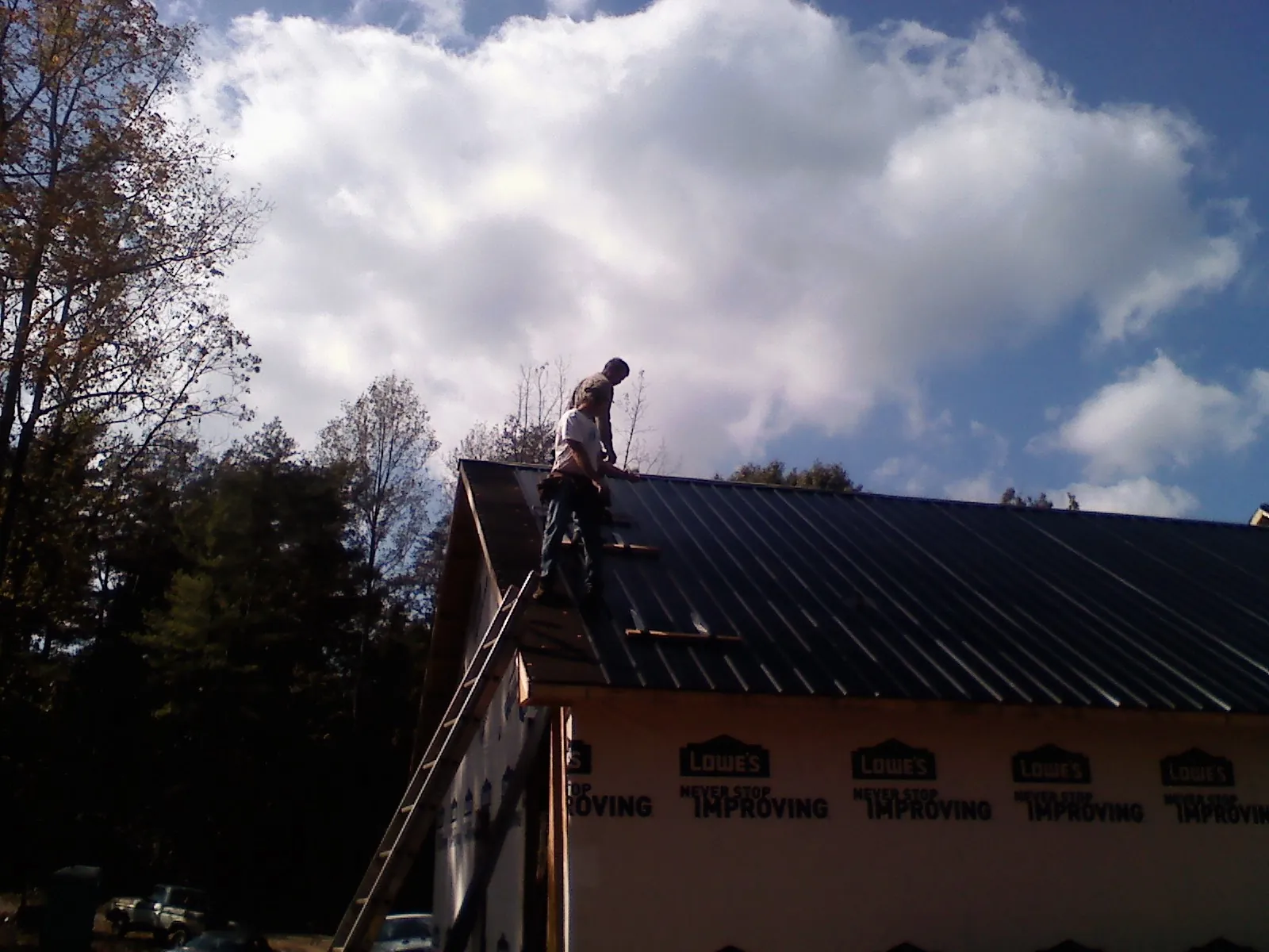 Roofer fastening dark metal panels high against a cloudy sky, from a Roof Inspection job in Blountville