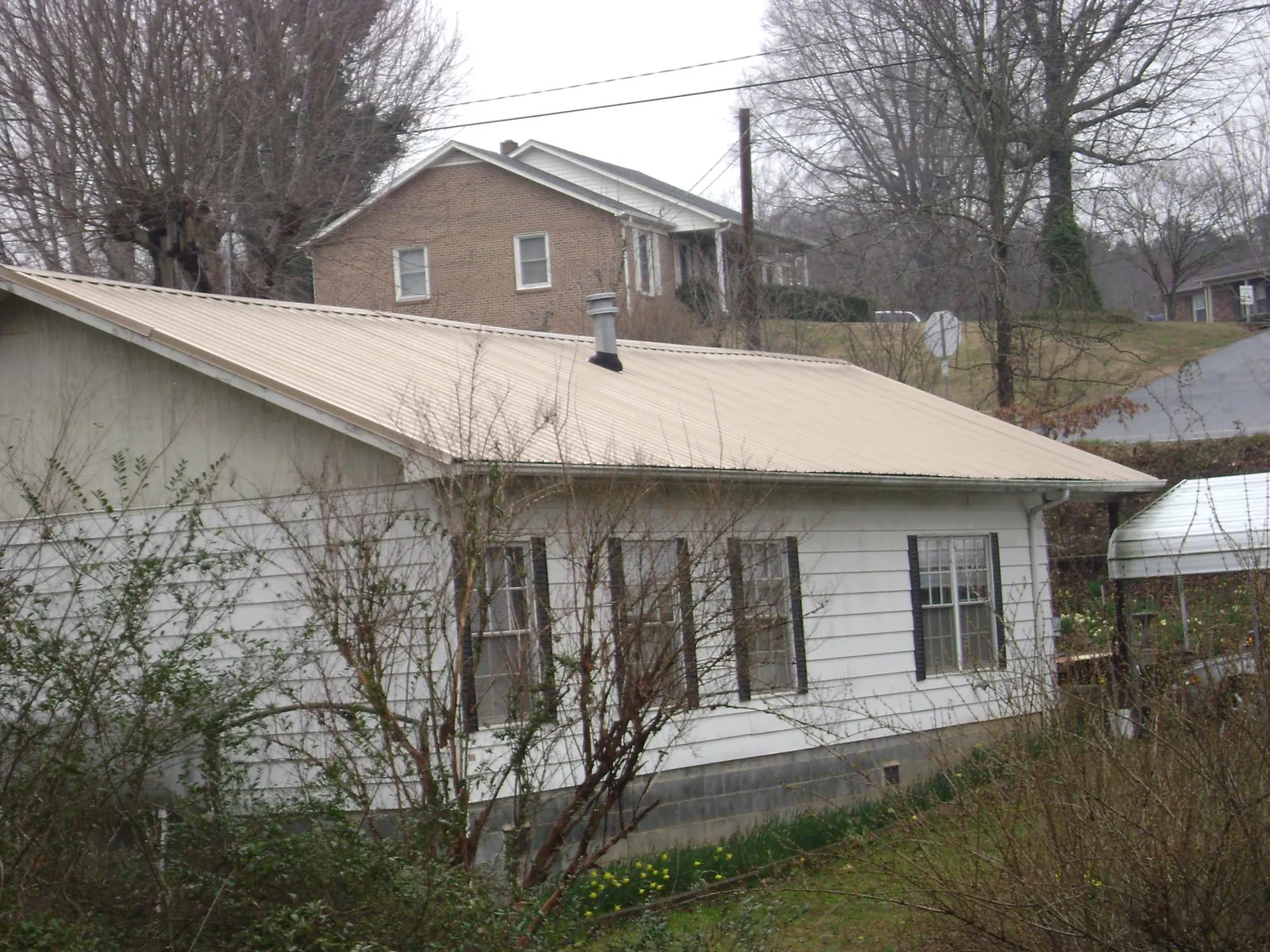 Tan metal roof on a white sided house set into a hillside — Commercial Roofing by Roofing Brothers in Blountville